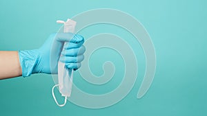 One hand in medical gloves or latex gloves holding face mask isolated on blue and green or Tiffany Blue color background