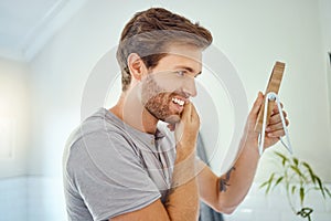 One handsome man checking his teeth in a bathroom at home. Caucasian male cleaning his teeth and looking in a mirror in