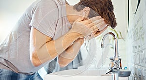One handsome man washing his face in a bathroom at home. Caucasian male using a face wash to prevent breakout, acne and