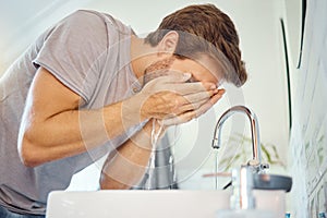 One handsome man washing his face in a bathroom at home. Caucasian male using a face wash to prevent breakout, acne and