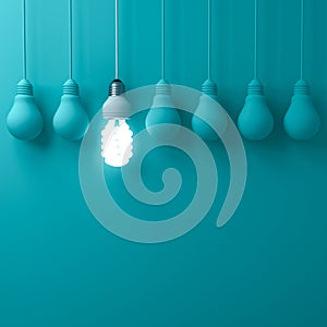 One hanging eco energy saving light bulb glowing and standing out from unlit incandescent bulbs on dark green pastel color