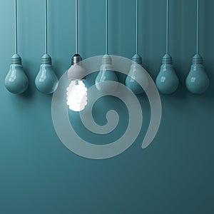 One hanging eco energy saving light bulb glowing and standing out from unlit incandescent bulbs photo