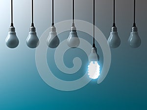 One hanging eco energy saving light bulb glowing and standing out from unlit light bulbs on dark green blue background