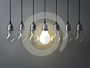 One hanging light bulb glowing different and standing out from unlit incandescent bulbs