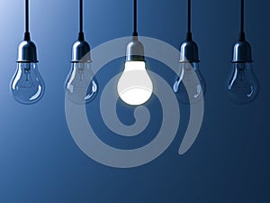 One hanging light bulb glowing different and standing out from unlit incandescent bulbs with reflection on dark blue background