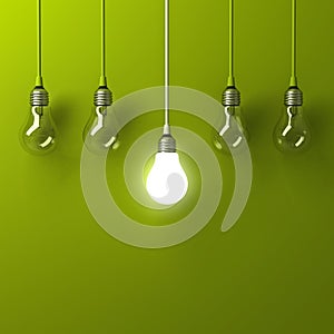 One hanging light bulb glowing different and standing out from unlit incandescent bulbs with reflection on green background