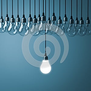 One hanging light bulb glowing with unlit incandescent bulbs on dark cyan background