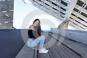 One happy beautiful woman in long hair sitting on staircase at promenade while smiling and looking camera