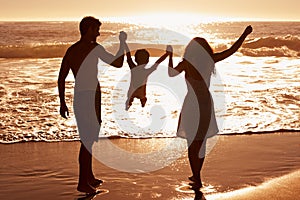 One happy family. Rear-view of a couple swinging their child between them as they walk on the beach at sunset.