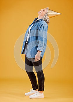 One happy mature caucasian woman wearing a birthday hat while posing against a yellow background in the studio. Smiling