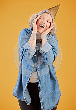 One happy mature caucasian woman wearing a birthday hat while posing against a yellow background in the studio. Smiling