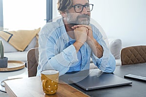 One happy and serene man looking up the air at home with closed laptop on the table. Concept of dreamer and daydreaming people.