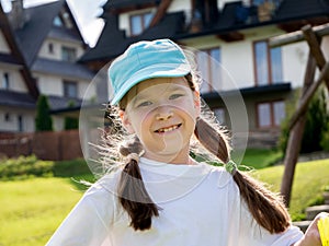 One happy young elementary school age child, cheerful girl smiling in the sun, simple outdoors portrait, kid in a baseball cap