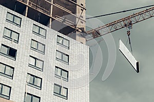 One high-rise crane hauling glare plate against a house and gray sky