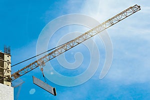 One high-rise with glare crane hauling plate against a house and sunny blue sky during the construction phase.