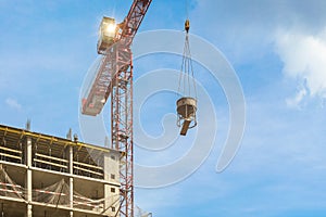 One high-rise red crane with flare against a house and sky during the construction phase