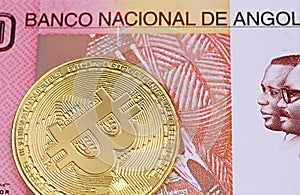 A one hundred Angolan kwanza bank note with a golden physical Bitcoin