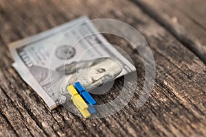 One hundred dollar banknote on a blue and yellow clothespins on wooden background. Macro.