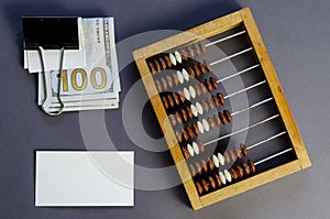 One Hundred Dollar Bill Sandwiched Binder Clip, Blank Business Card, and Old Wooden Abacus on Gray Background