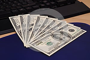 One hundred dollar bills fanned out on a computer keyboard