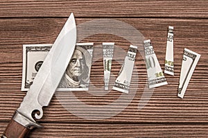 A one hundred dollar denomination cut into pieces using a knife against the background