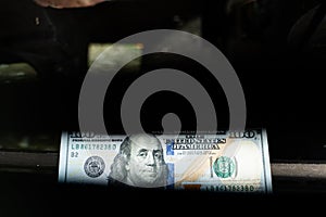 A one hundred dollar denomination of the United States of America is seen through a slot against a dark background. Symbolization photo