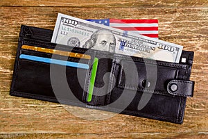 One hundred dollars banknote reach out out of a black old purse.