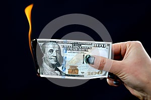 One hundred dollars are burning with fire in hand on a black