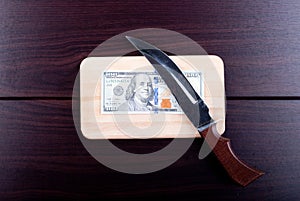 One hundred dollars on a cutting board with a knife, top view photo