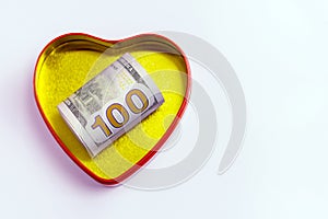 One hundred dollars in a gold heart shaped box with a red outline against a light background. Concept for the holiday St. Valentin