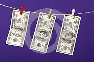 One hundred dollars hanging on clothesline with wooden clips on blue background
