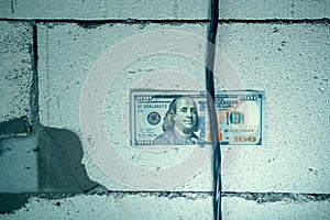 One hundred dollars is inserted between a thick black electrical wire and a wall of aerated concrete bricks.Bribery and corruption
