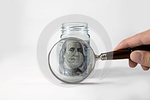 One hundred dollars under a magnifying glass, close-up. The person examines the money in the piggy bank