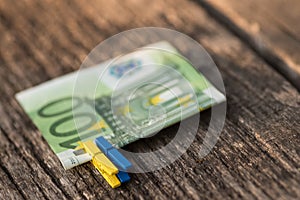 One hundred euro banknote on a blue and yellow clothespins on wooden background. Macro.