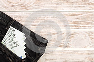 One hundred euro banknotes in a jeans pocket on white wooden background with copy space for your text. Top view