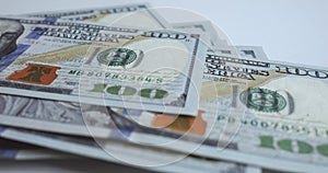 One hundred US dollar bills are neatly laid on white table. Close-up shows details of banknotes: portraits, ornaments