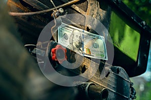One hundred us dollars on a diesel engine of a minitractor close-up. Money and the agricultural industry. Maintenance and repair