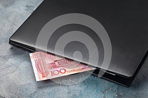 One hundred yuan sticking out of a laptop, concept on the theme of remote work