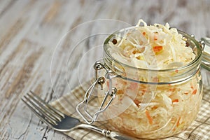 One jar of sauerkraut and carrots in its own juice with spices on a light, white wooden table, a vertical kind of cabbage in a jar