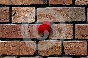 One knitted red heart on a crumbling old red brick textured wall