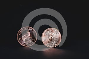 One Krugerrand and a dollar gold coin stand side by side on a dark background