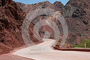 A one lane road that is winding down a mountainous area with many red colored rocks
