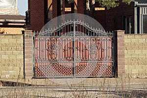 One large brown closed metal gate with a black wrought iron pattern and part of a brick wall