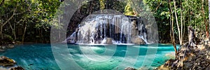 One of the largest waterfalls in Erawan National park in Thailand with trees on the left has a milky pool with some fish