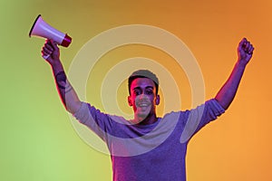 One Latina young man with megaphone, loudspeaker standing hands up isolated on gradient yellow green background in neon