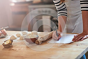 One learns by doing. Cropped shot of a woman writing a recipe for the dough that shes preparing.