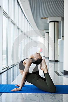 One-Legged King Pigeon Pose. Woman yoga practice pose training concept in gym hall with big windows photo