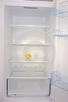 One lemon in open empty refrigerator.