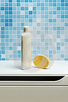 One liter bottle of shampoo with a yellow synthetic sponge on a white bathroom cabinet and blue tiles