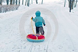 One little boy in winter runs along the snowy road alone. child pulls sled